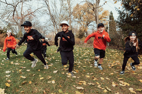 STY House: a group of kids wearing STY House gear running through leaves